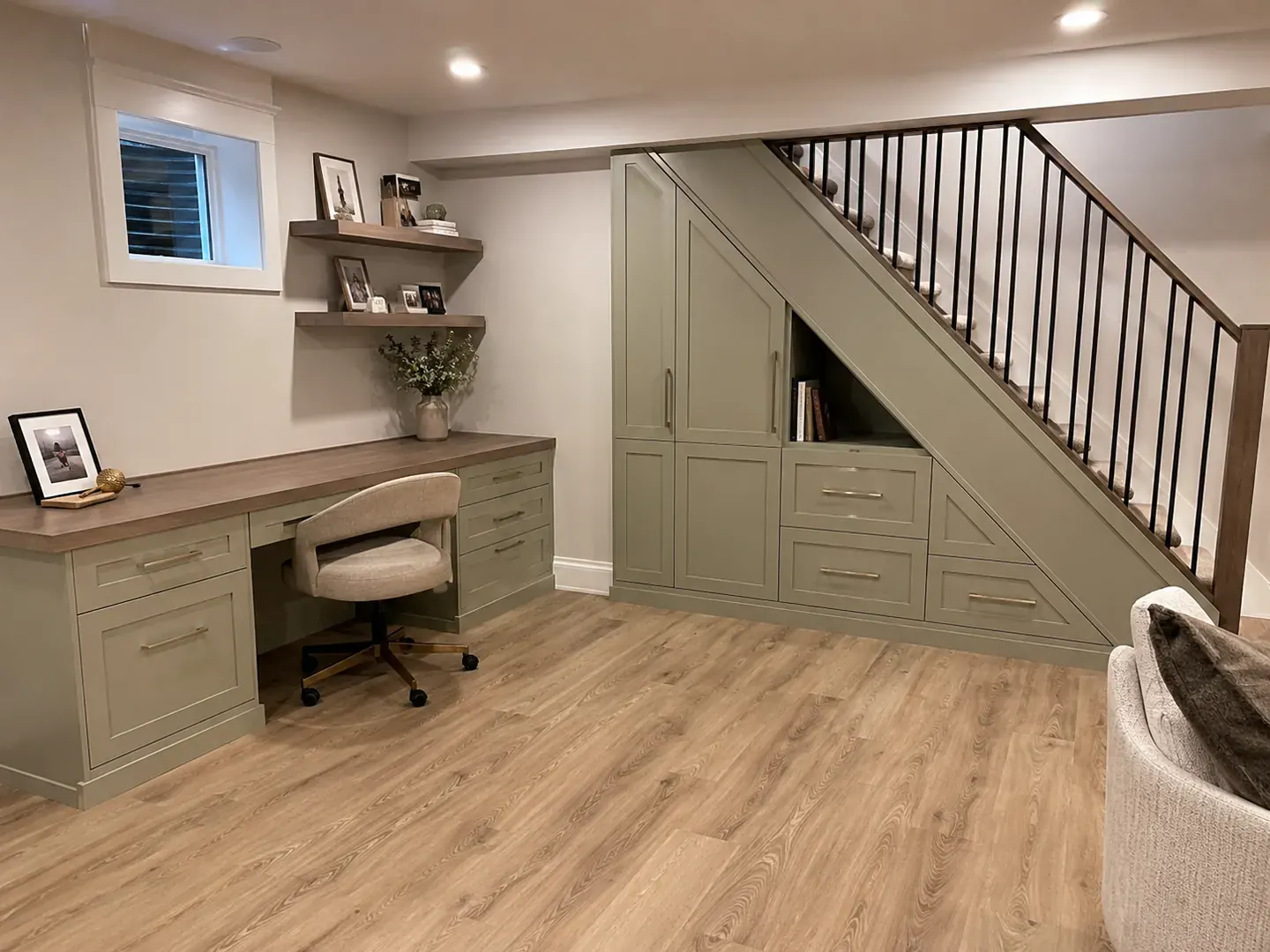 Finished basement study with a built-in desk, sage cabinetry, and storage under the stairs