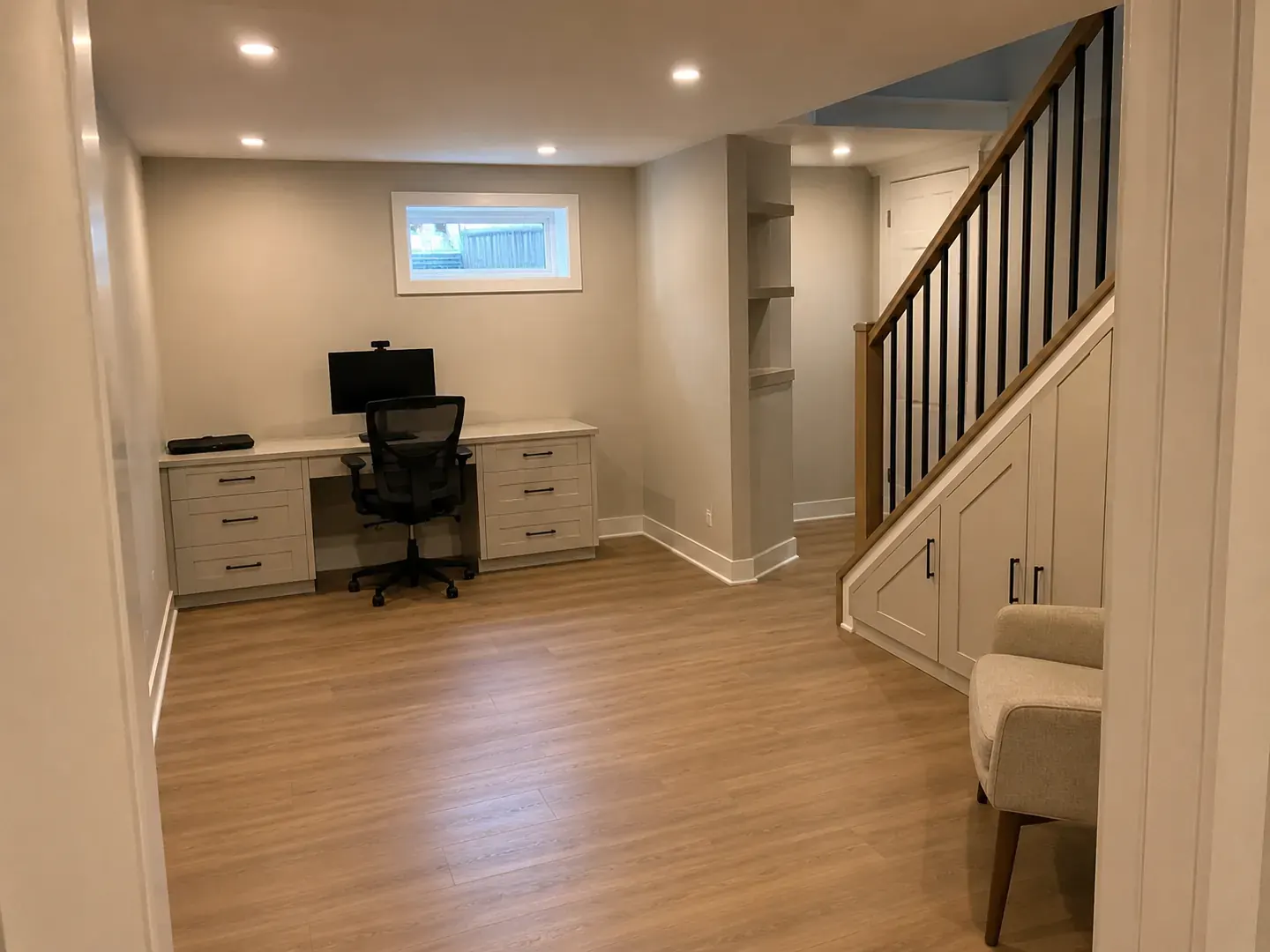 Finished basement office nook with a built-in desk beside a black railed staircase