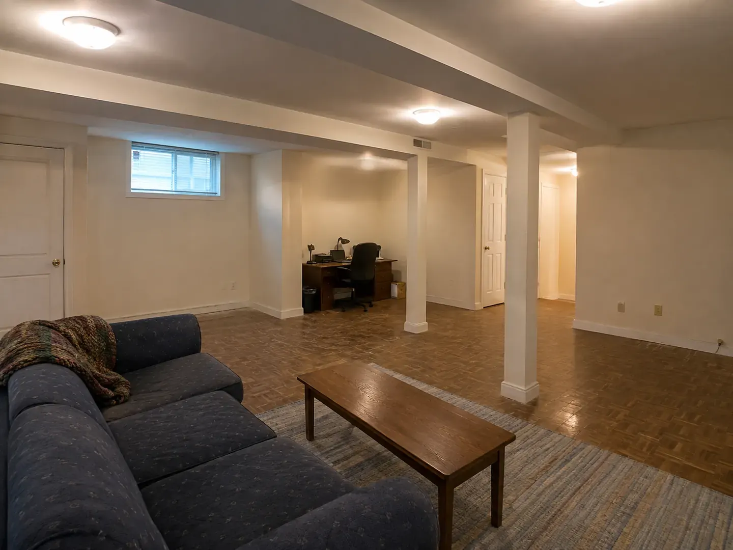 Before: a dark, dated lower level with worn flooring and exposed support columns