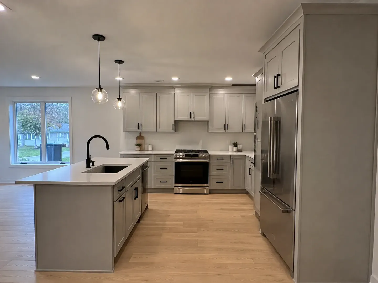 Renovated Toronto kitchen with grey green shaker cabinetry, glass globe pendants, and a garden window