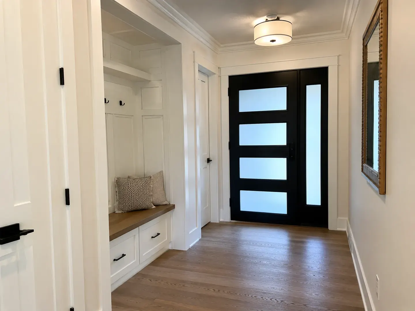 Renovated Toronto home entryway with a built-in mudroom bench, oak flooring, and a black glazed front door